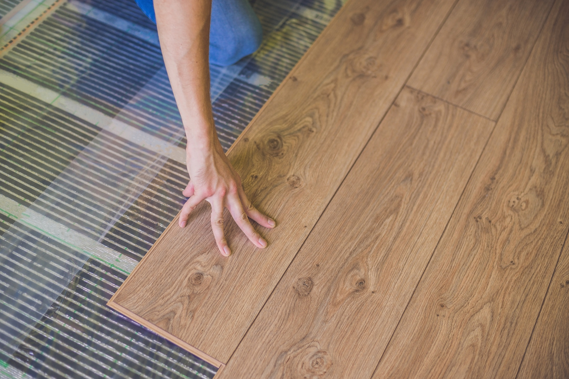 Man Installing New Wooden Laminate Flooring. Infrared Floor Heating System under Laminate Floor